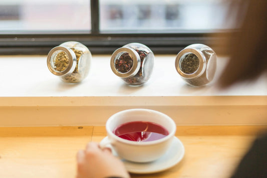 Liver health and herbal teas with jars of dried herbs and a cup of herbal tea on a table.