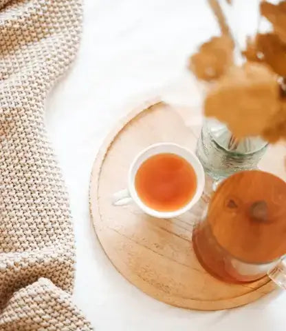 A cozy scene featuring a cup of anti-inflammatory tea and glass teapot on a wooden tray.