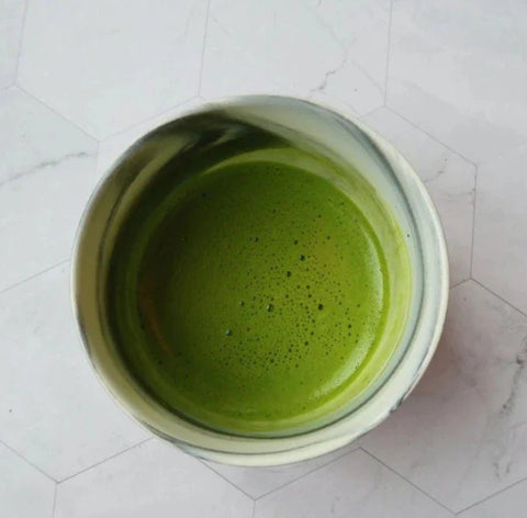 Green Matcha in a white cup on a light gray tiled surface