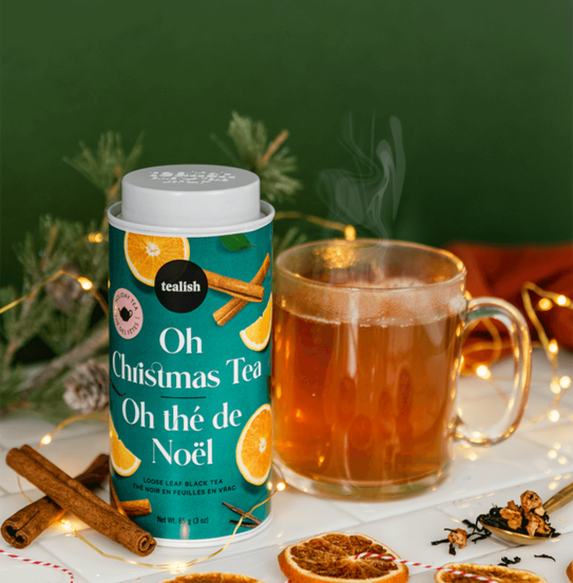 Festive Oh Christmas Blend tea canister beside a steaming cup, surrounded by holiday decorations and spices.