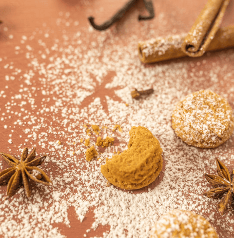 Gingerbread cookies scattered with powdered sugar, surrounded by cinnamon sticks and star anise on a festive surface.