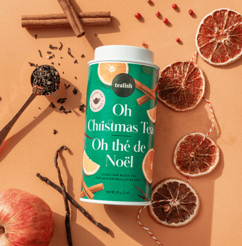 Oh Christmas Blend tea canister surrounded by spices, dried fruits, and loose black tea, exuding festive flavors.