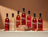 Eight bottles of Proper Natural Syrups including Caramel Syrup, set against a warm background with sugar.