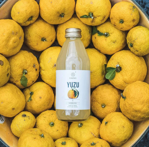 Bottle of Yuzu Sparkling Juice amidst fresh Yuzu fruits, highlighting its natural ingredients and Japanese origin.