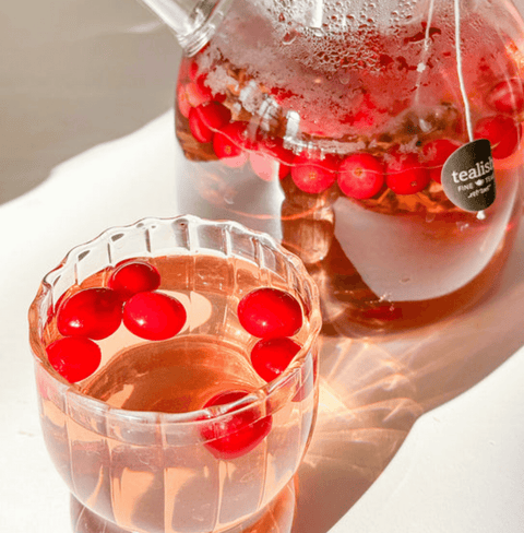 Glass teapot and cup filled with cranberry-infused herbal tea, featuring vibrant red cranberries floating on top.