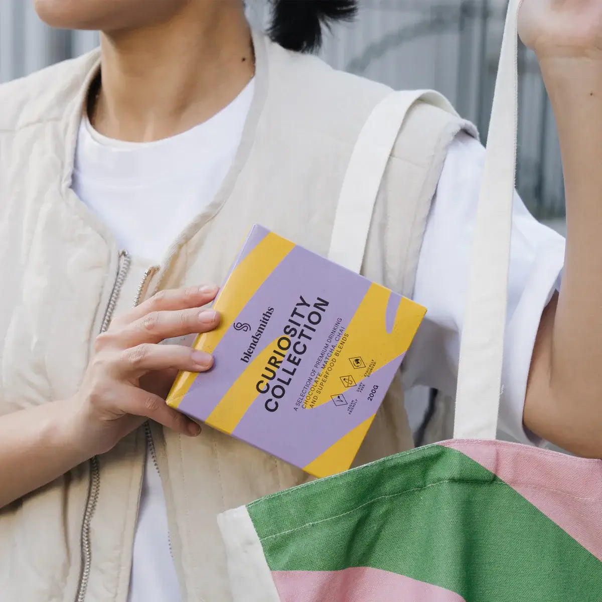 A vibrant display of Blendsmiths' Curiosity Collection, a selection of premium drinking chocolate, matcha chai, and superfood blends. A hand is holding a Japanese Matcha Blend sachet, while a stack of other flavored sachets, including Original Choc Blend,