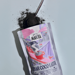 Image of Char-coco Latte powder package with activated charcoal on a spoon, promoting a detox beverage experience.