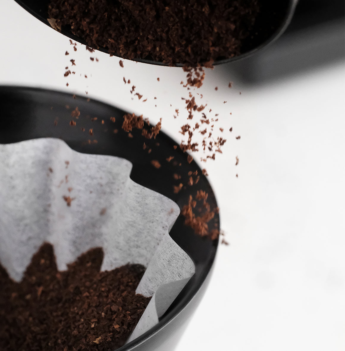 Pouring ground coffee into a FLO 55 Paper Filters 100x, ideal for rich and bright brew options.