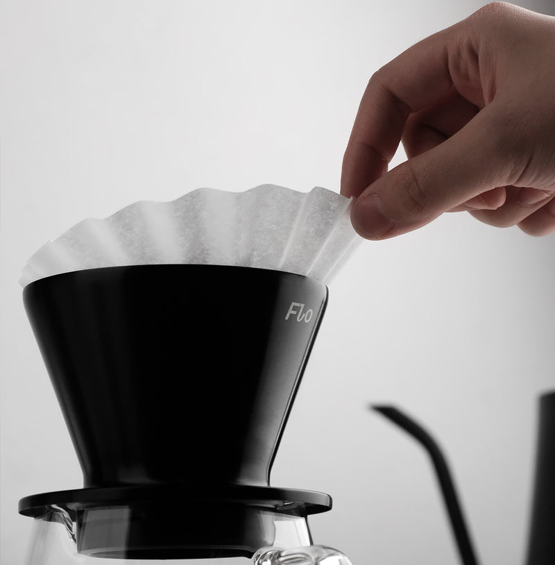 A hand placing a FLO 55 Paper Filter 100x into a brewing cone for coffee extraction.