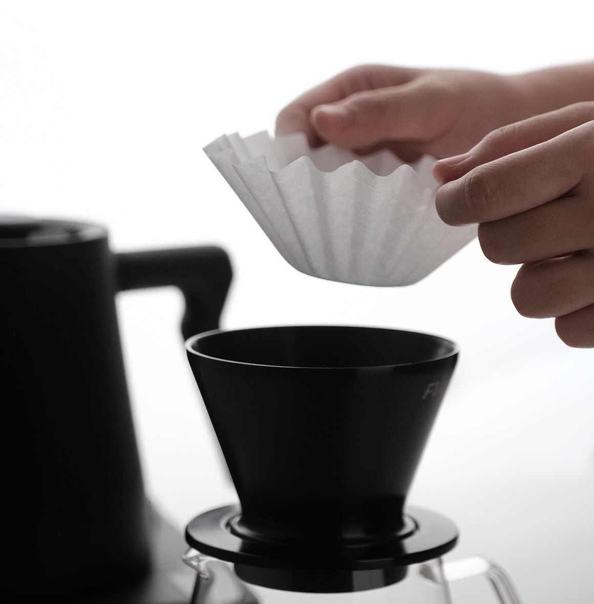 Person placing a FLO 55 Paper Filter 100x into a black coffee dripper for brewing.