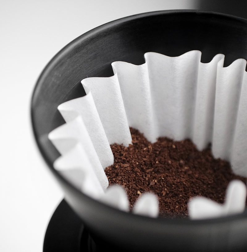 Close-up of FLO 55 Paper Filters 100x in a flat-bottom brewer with coffee grounds for brewing.