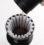 Pouring ground coffee into FLO 85 Paper Filters 100x for brewing precision and flavor.