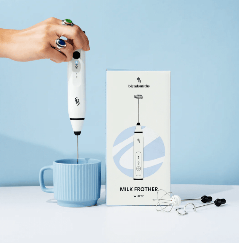 Blendsmiths Handheld Milk Frother creating foam in blue cup with packaging and accessories on display.