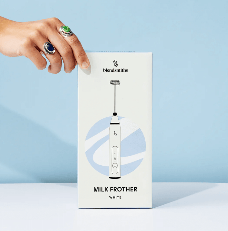 Handheld Milk Frother by Blendsmiths in packaging with a hand reaching for it, ideal for creating café-style beverages at home.
