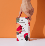 Hand holding a pack of Chilli Chocolate Blend with vibrant packaging against an orange background.