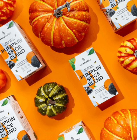 Pumpkin Spice Blend packages arranged with decorative pumpkins on an orange background, highlighting warm, authentic flavors.