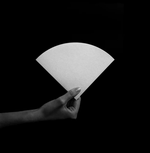 Hand holding Sibarist Fast - Cone Specialty Coffee Paper Filter against black background