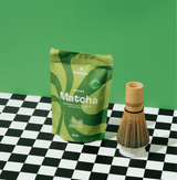 Wakaba Matcha packaging with a bamboo whisk on a checkerboard surface, ideal for matcha lovers.