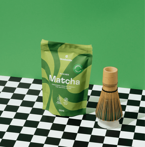 Wakaba Matcha packaging with a bamboo whisk on a checkerboard surface, ideal for matcha lovers.