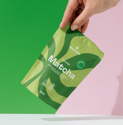 Hand holding a package of Wakaba Ceremonial Matcha against a green and pink background.