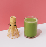 Glass of Wakaba Ceremonial Matcha with bamboo whisk against a pink background