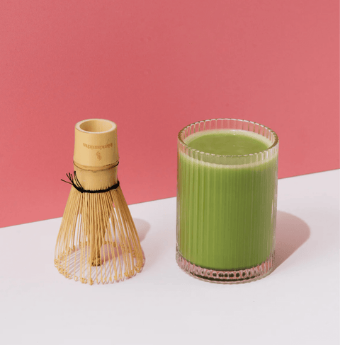 Glass of Wakaba Ceremonial Matcha with bamboo whisk against a pink background