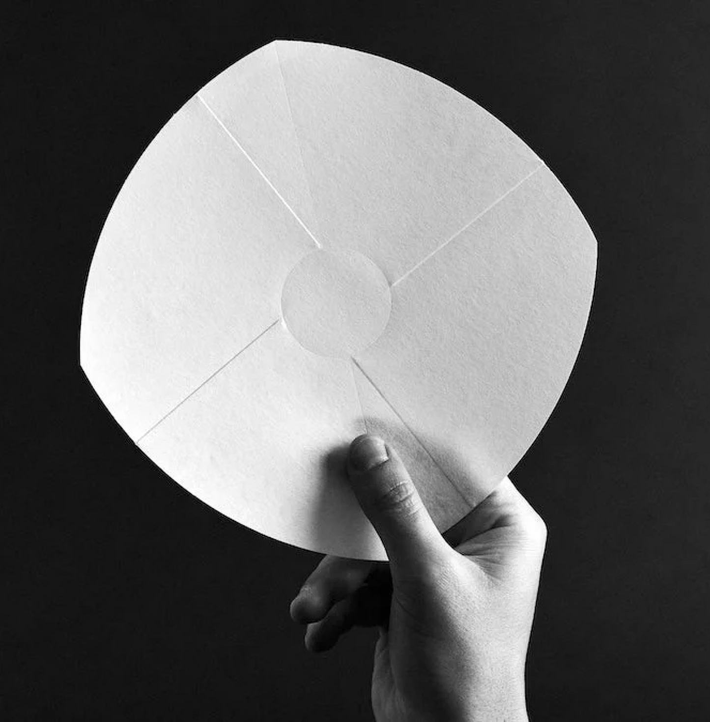 Hand holding Sibarist B3 Flat Coffee Filter Paper against black background, highlighting its flat-bottomed design for better coffee clarity.