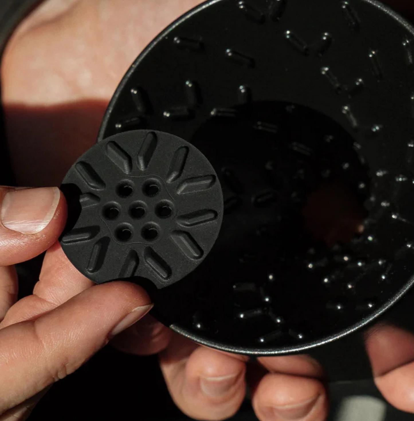 Graycano Coin being inserted into a dripper, optimizing water flow and temperature for improved coffee brewing performance.