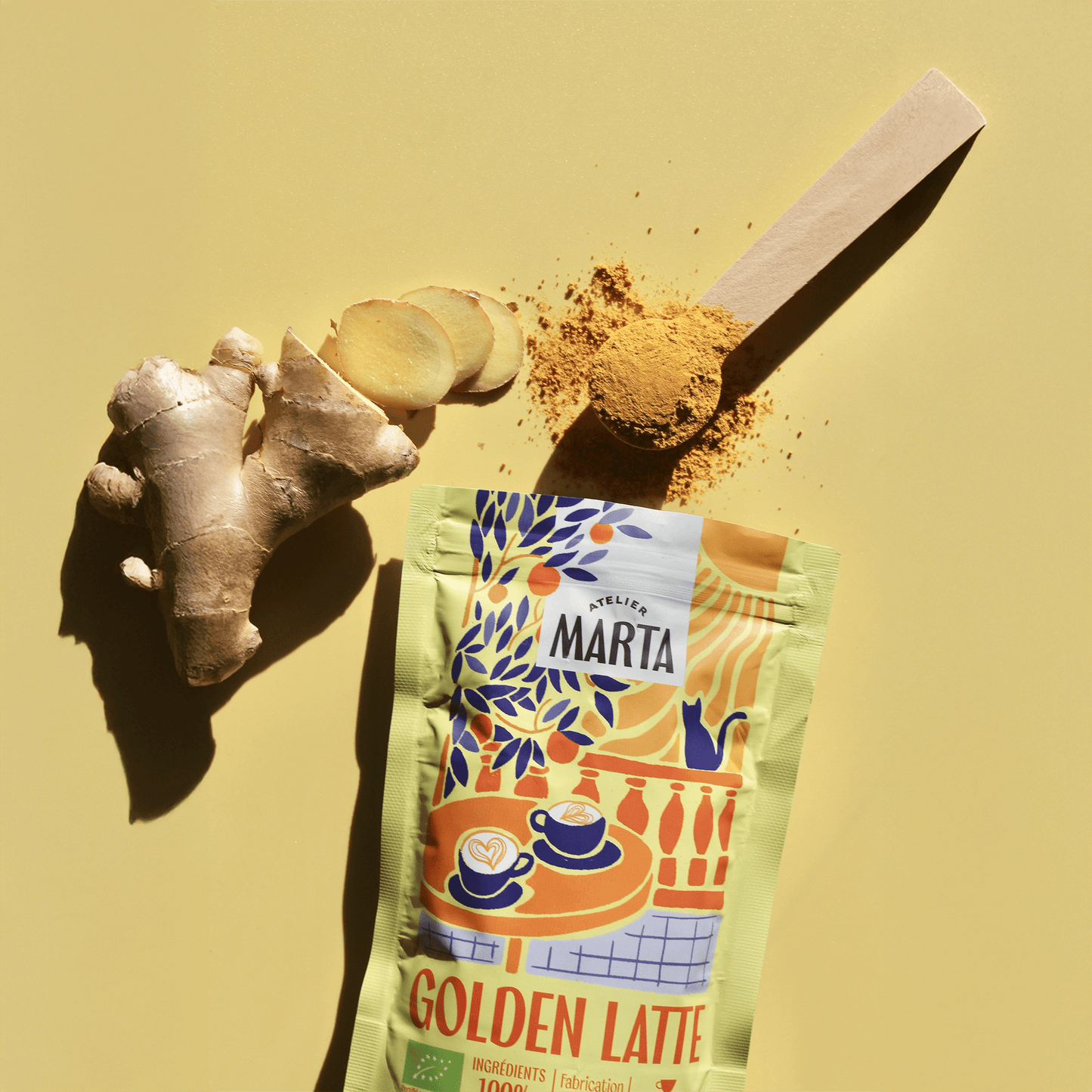 Organic Golden Latte from Atelier Marta with turmeric, ginger slices, and measuring spoon on yellow background.