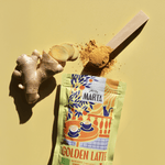 Organic Golden Latte from Atelier Marta with turmeric, ginger slices, and measuring spoon on yellow background.