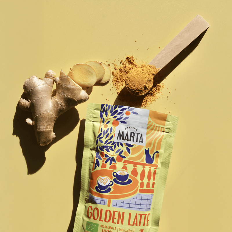 Organic Golden Latte from Atelier Marta with turmeric, ginger slices, and measuring spoon on yellow background.