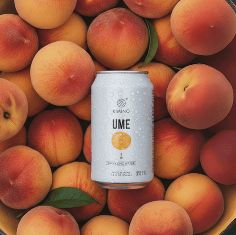 Can of Ume Sparkling Water by Kimino surrounded by fresh Japanese plums, showcasing a refreshing, sugar-free beverage option.
