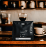 Bag of Black Forest coffee on a rustic cafe counter, surrounded by coffee cups and a warm, inviting atmosphere.