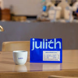 Blue julith coffee package with a white cup on a wooden surface