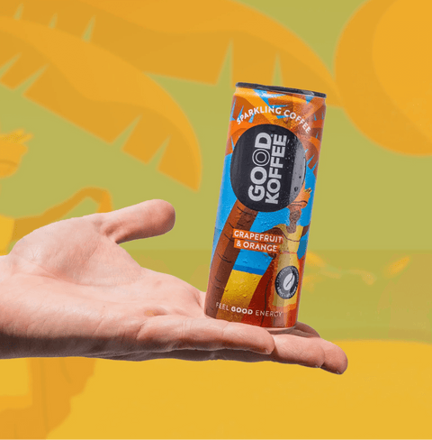 Hand holding a can of Grapefruit & Orange Sparkling Coffee - Barbados by Good Koffee, displayed against a vibrant tropical backdrop.