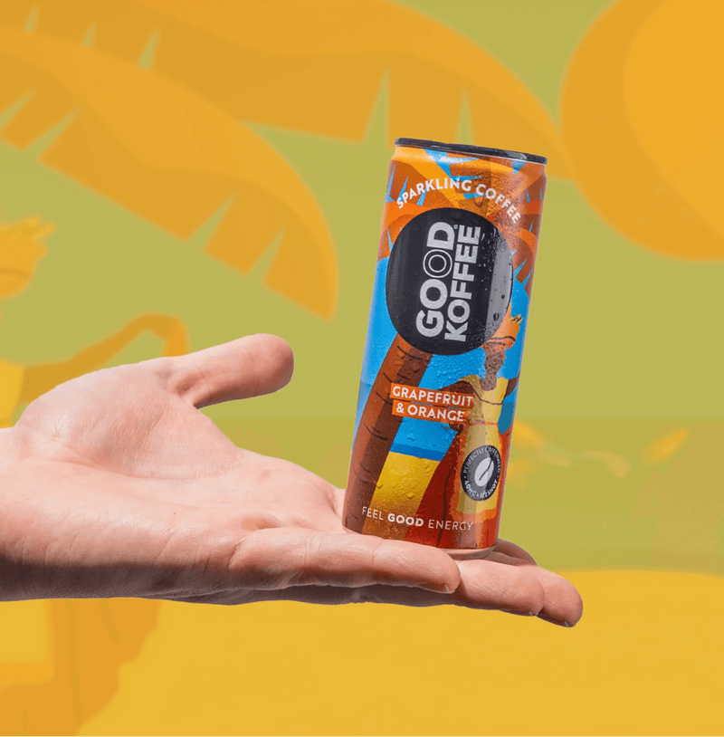 Hand holding a can of Grapefruit & Orange Sparkling Coffee - Barbados by Good Koffee, displayed against a vibrant tropical backdrop.