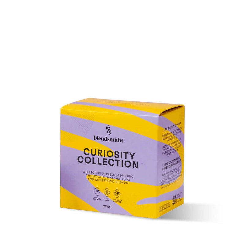 A vibrant display of Blendsmiths' Curiosity Collection, a selection of premium drinking chocolate, matcha chai, and superfood blends. A hand is holding a Japanese Matcha Blend sachet, while a stack of other flavored sachets, including Original Choc Blend,
