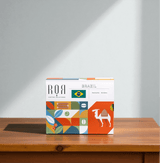 Drip Bag Box - Brazil on wooden table with colorful packaging and sunlight highlighting the premium coffee product.