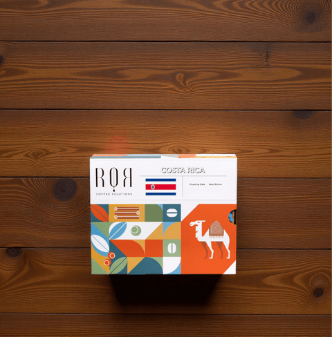 Drip Bag Box - Costa Rica on wooden table, showcasing vibrant packaging with abstract designs and Costa Rican flag.