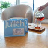 Person pouring tea into a glass with 'julith' packaging on a wooden table.