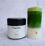 Clarity Koicha matcha green tea powder in a double-walled glass bowl beside a ceremonial matcha tin, smooth and vibrant in color.