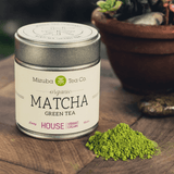 House Organic Matcha Green Tea tin with vibrant green matcha powder on wooden surface.