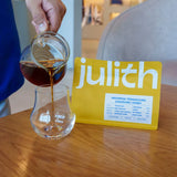 Person pouring honey into a glass with a 'julith' product card in the background.
