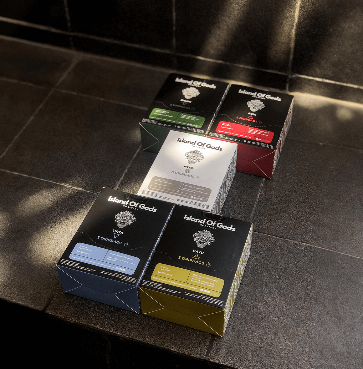 Variety of Island of Gods drip bag coffee boxes displayed on a rustic surface, showcasing vibrant packaging and flavors.