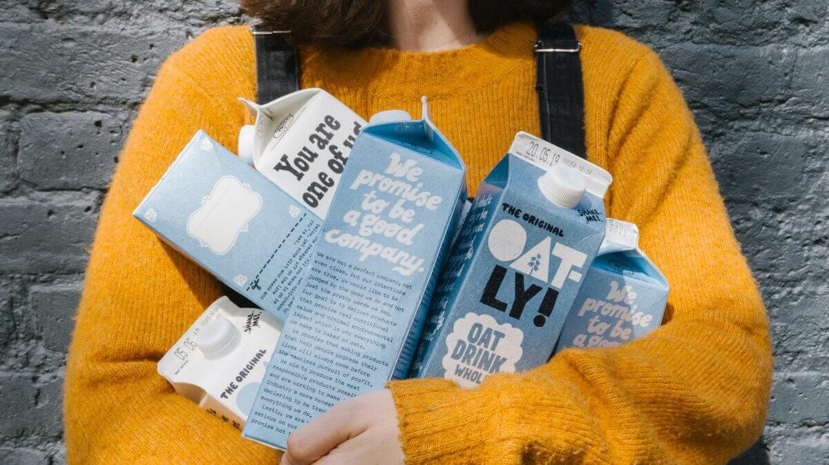 A person in a bright sweater holds oat drink cartons, showcasing the vibrant packaging of plant-based beverages.