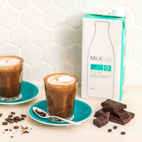 Coconut Milk latte served in clear glass with chocolate on the side, featuring MILKLAB coconut milk packaging.