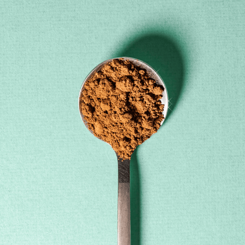 A stainless steel spoon filled with Mint Chocolate powder on a green background.