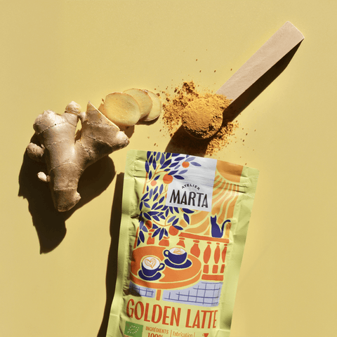 Organic Golden Latte from Atelier Marta with turmeric, ginger slices, and measuring spoon on yellow background.