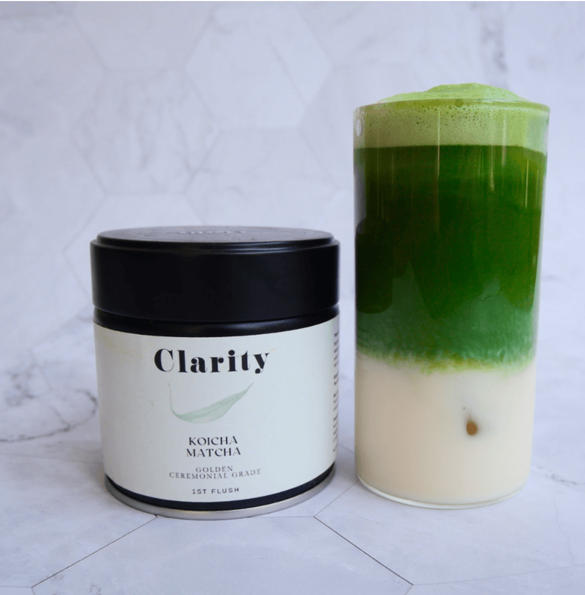 Clarity Koicha matcha green tea powder in a double-walled glass bowl beside a ceremonial matcha tin, smooth and vibrant in color.