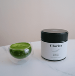 Clarity Koicha matcha green tea powder in a double-walled glass bowl beside a ceremonial matcha tin, smooth and vibrant in color.